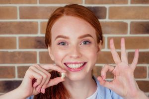 a red-haired woman smiles holding a tooth