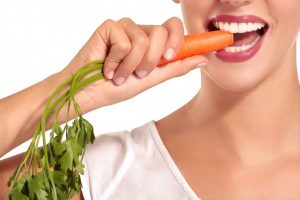 a woman with nice teeth bites a carrot